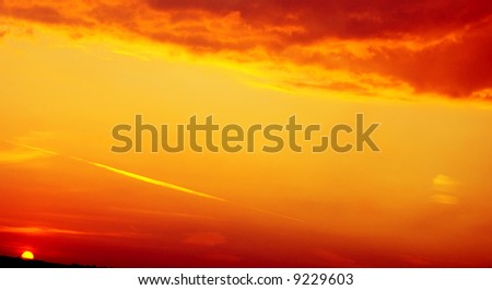 A landscape. The storm clouds shined by bright red light of the coming sun. The strip of the pure sky is crossed with a trace of the plane.