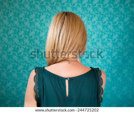 Back of a woman\'s head standing in front of a wallpapered wall
