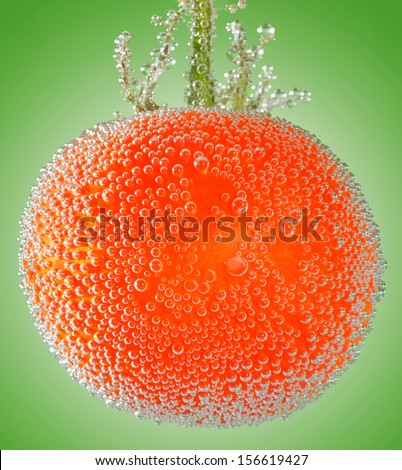 A fresh organic tomato immersed in mineral water on green background