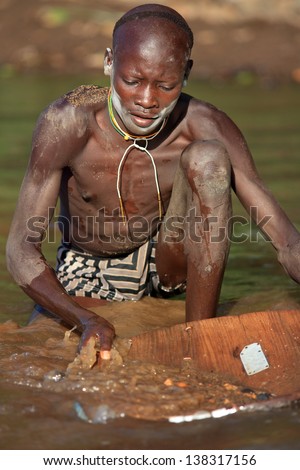 SOUTH OMO - ETHIOPIA - OCTOBER 21, : Unidentified Suri man digging gold on October 21, 2012 in South Omo, Ethiopia. A 5-year resettlement program started 2011 threatens tribes in Ethiopia.