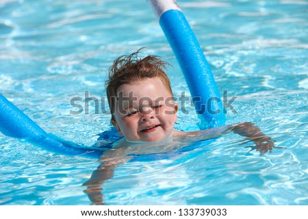 Happy little boy learning to swim with pool noodle