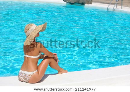 Young woman in hat sitting on the ledge of the pool.