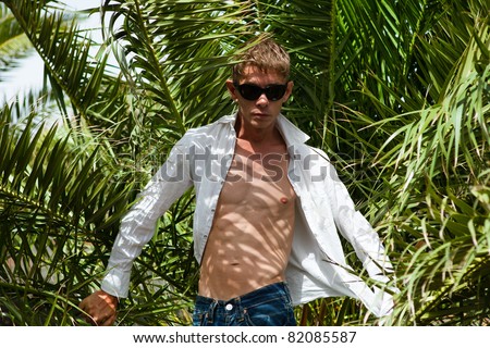 Young sexy man in sunglasses among palm trees on a windy day
