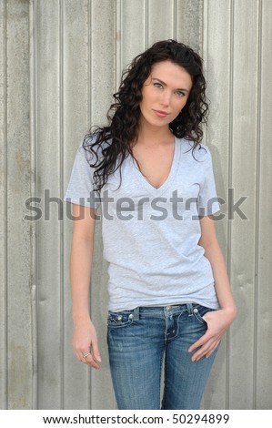 Beautiful, young, brunette female model posing in gray t-shirt and jeans in front of silver, metal wall.