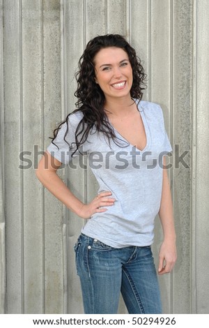 Beautiful, young, brunette female model posing in gray t-shirt and jeans in front of silver, metal wall.