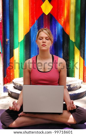 Young pretty blond woman in yoga lotus position outdoors in park with silver laptop computer on lap.