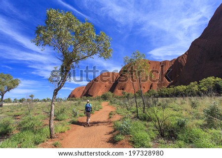 South Eastern side of Uluru set against a bold blue sky with one tree and a person walking on the track