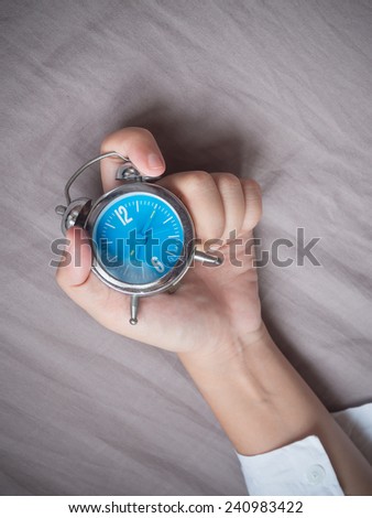 Hand grabing alarm clock on bed background