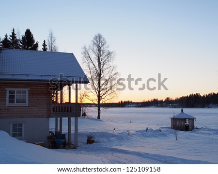 Winter landscape with the river in frosty day. Old wooden rural house situated on the bank of the river