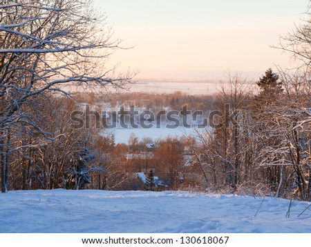 Beautiful winter sunset with trees in the snow.  View from the hill on the village, the snow-covered wood and the lake