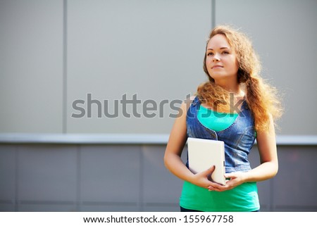 Pretty smiling young girl holding a tablet computer on the background office building