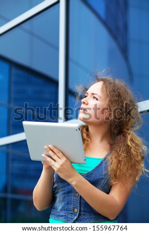 Pretty smiling young girl working on a tablet computer on the background of office building