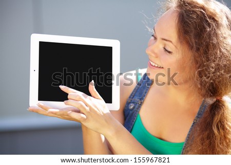 Pretty smiling young woman is showing a tablet computer on a gray background