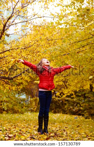 A teenage girl is walking in the park in autumn with yellow leaves arms outstretched