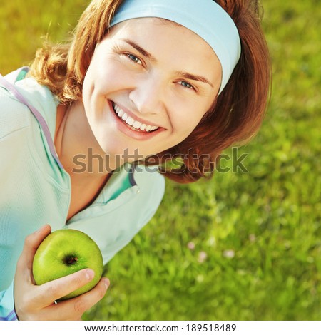 Portrait of sporty smiling woman with green apple on a grass background. outdoor sports