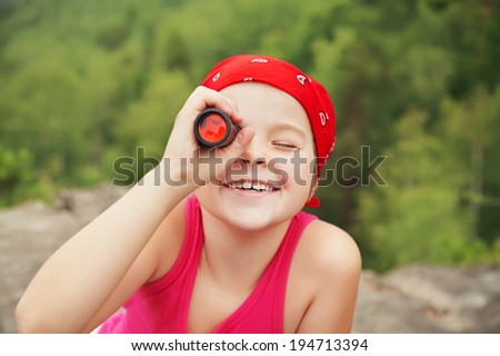 funny little girl in a bandana with a spyglass. children outdoors