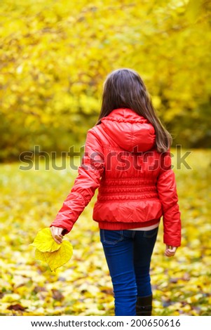 A teenage girl is walking in the park in autumn with yellow leaves