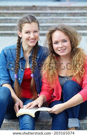 Two friends reading a book on the steps of the University.  youth lifestyle