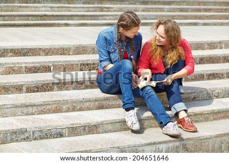 Two friends reading a book on the steps of the University.  youth lifestyle
