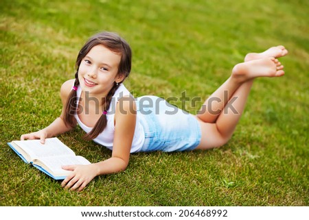 girl lying on the grass in the park and reading a book. reading, learning and education