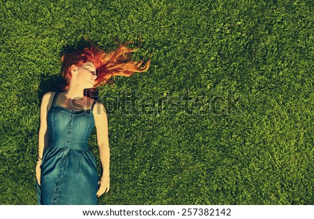 redhead girl relaxing lying on the grass. woman relaxation outdoor. photo with artistic effect. vintage toning. film retro style