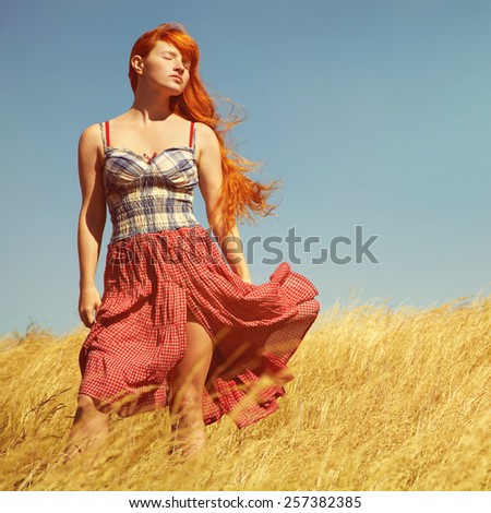 sexy redhead woman in a dress outdoors. Beautiful stylish romantic young girl on nature background. field and clear cloudless sky