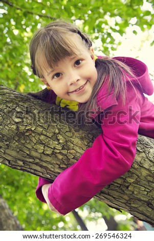 Funny playful little girl sitting on a tree in the park. children outdoors. vacation in the summer park