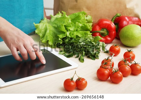 young housewife uses a tablet computer in the kitchen. woman following recipe cooking vegetables on digital tablet. online food shopping