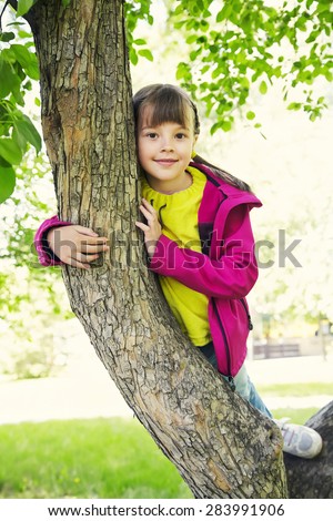 Funny playful little girl sitting on a tree in the park. children outdoors. vacation in the summer park