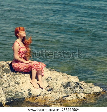 romantic redhead young woman in a dress on the ocean coast. girl in the summer outdoors. concept of freedom, inspiration and dreams. sea