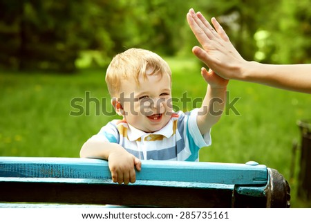 outdoor portrait of a boy on green background. happy child on walk in the summer park. Give five gesture support. high five