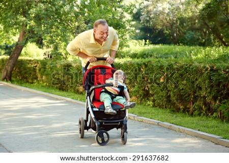 outdoor portrait of a happy father and son. baby sitting in stroller and dad walk in the summer park