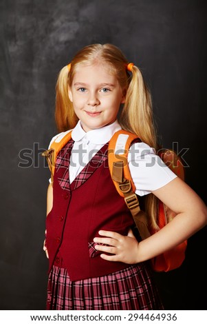 Portrait of a funny schoolgirl with schoolbag on blackboard background. School and education