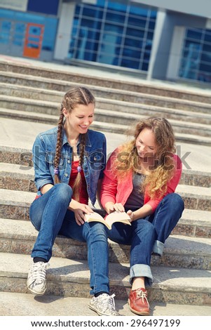 Two friends reading a book on the steps of the University. youth lifestyle. students girls