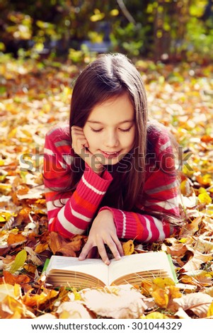 girl lying on fallen leaves  in the park and reading a book. reading, learning and education in autumn