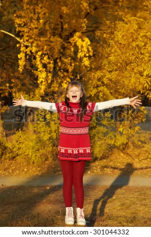 very happy little girl in the park in autumn with yellow leaves. adolescent with arms outstretched outdoor