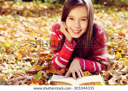 girl lying on fallen leaves  in the park and reading a book. reading, learning and education in autumn
