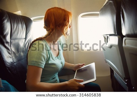 woman in the chair on board the aircraft. girl with tablet computer in an airplane. flight and travel