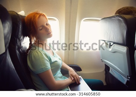 sleeping woman in the chair on board the aircraft. girl with tablet computer in an airplane. flight and travel