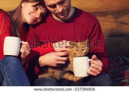 man and woman  drinking tea at his home. young couple in love with mugs in hands and cat