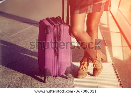 female legs closeup. stylish woman with a suitcase standing at the window at the airport. traveler waiting airplane flight