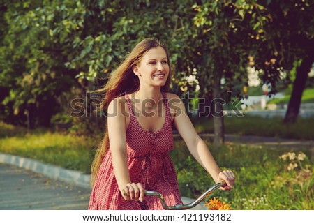 young woman in a dress rides a bike in a summer park