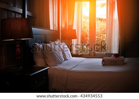 Bed maid-up with clean white pillows and bed sheets in beauty room. Close-up. Lens flair in sunlight. Sunrise garden view on the background