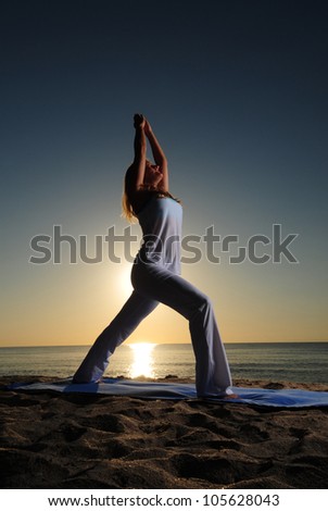 Woman doing Warrior I (Virabhadrasana I) yoga pose on beach during a beautiful sunrise