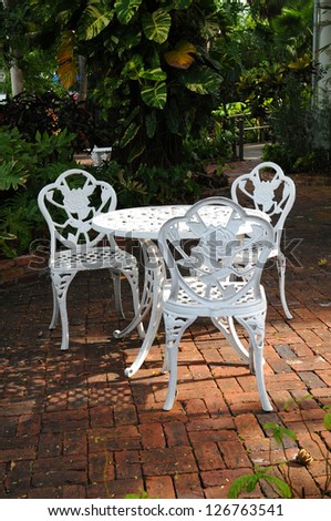 white ornamental garden chairs in a backyard patio with surrounding garden