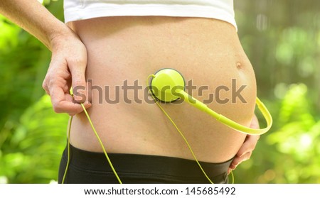 woman playing music for unborn baby with headphones on stomach during pregnancy