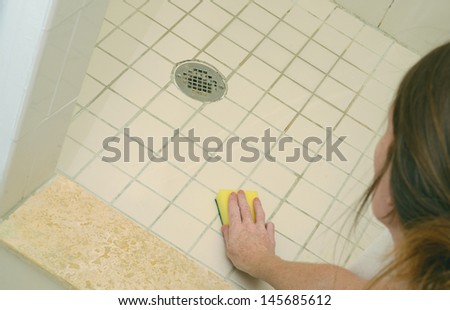 woman scrubbing soap scum from a dirty shower floor with scour pad