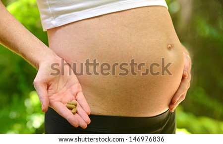 pregnant woman holding prenatal vitamins by stomach