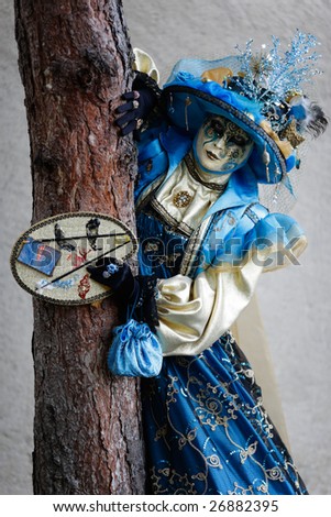 Woman carnival mask dressed in blue and yellow against a tree (Annecy/France)