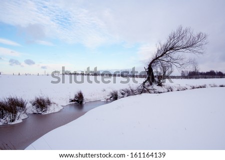 Picturesque and misty winter landscape with low sun, snow and partially ice on a narrow stream.